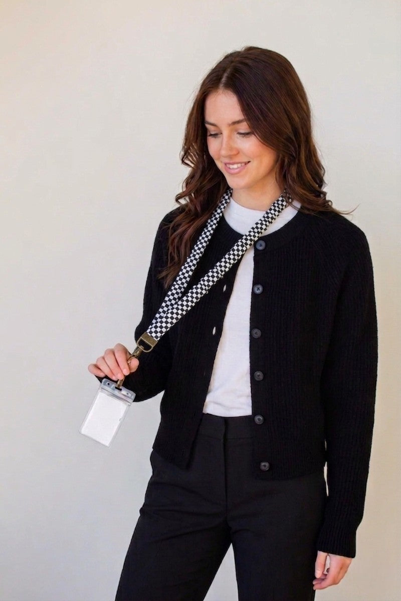 Woman wearing a black cardigan with a checkered bag over her shoulder against a plain background