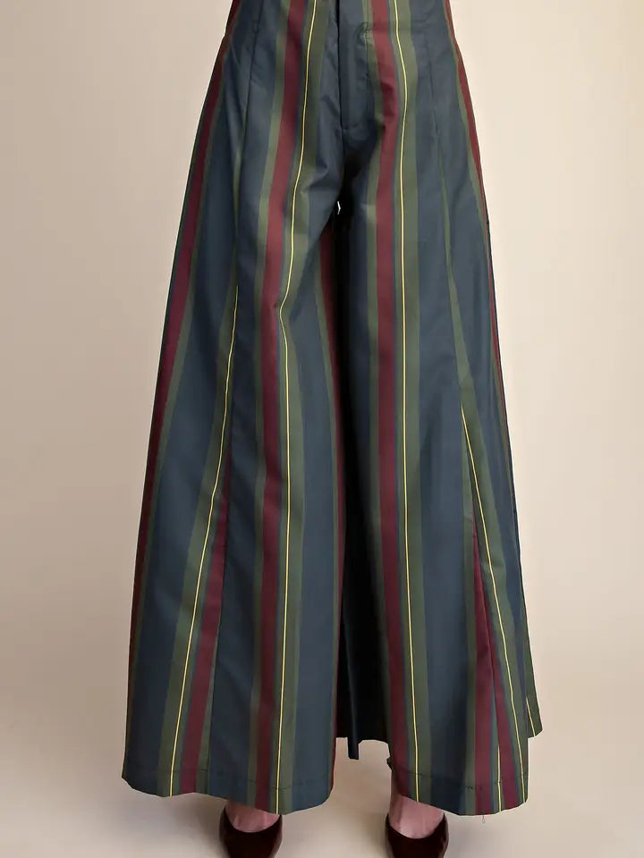 Wide-leg trousers with vertical stripes in dark teal, burgundy, olive green, and yellow, shown on a model from the waist down against a plain beige background.
