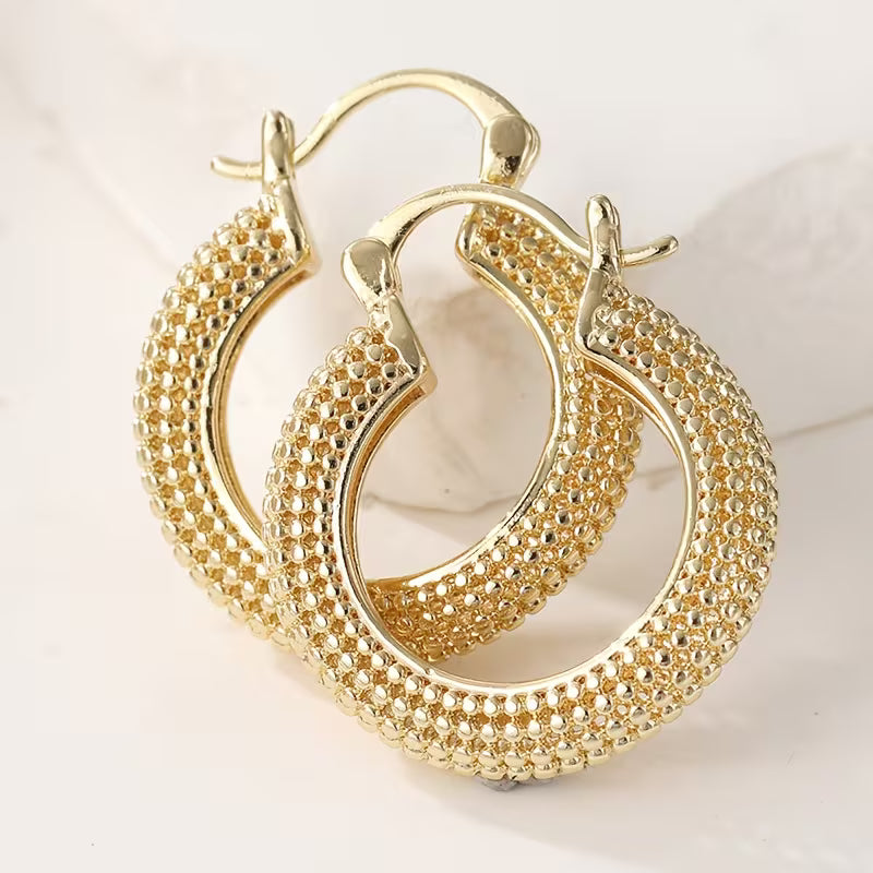 A pair of gold hoop earrings with a textured, beaded pavé-style finish, displayed on a clean white background.