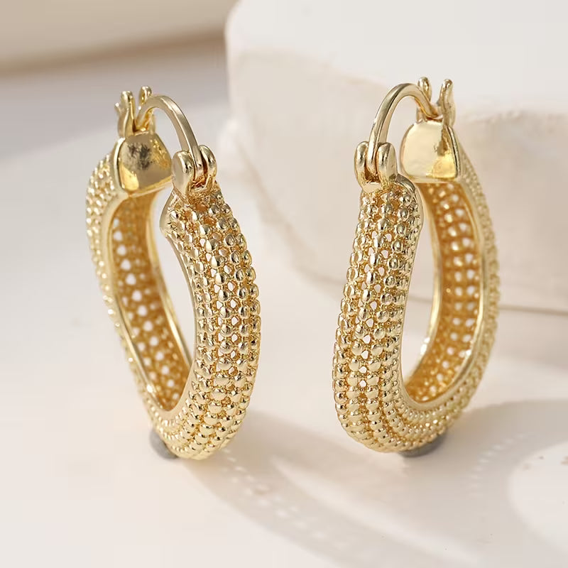 A pair of gold hoop earrings with a textured, pave-like beaded pattern on the outer surface, displayed on a clean white surface.