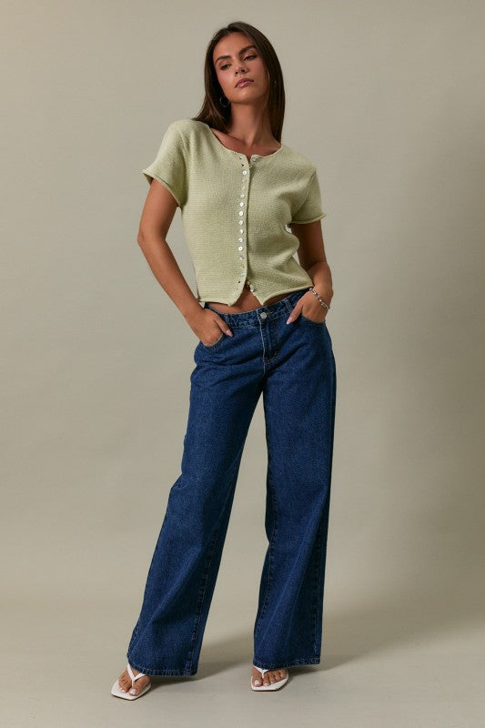 Woman wearing a green top and blue jeans against a beige background