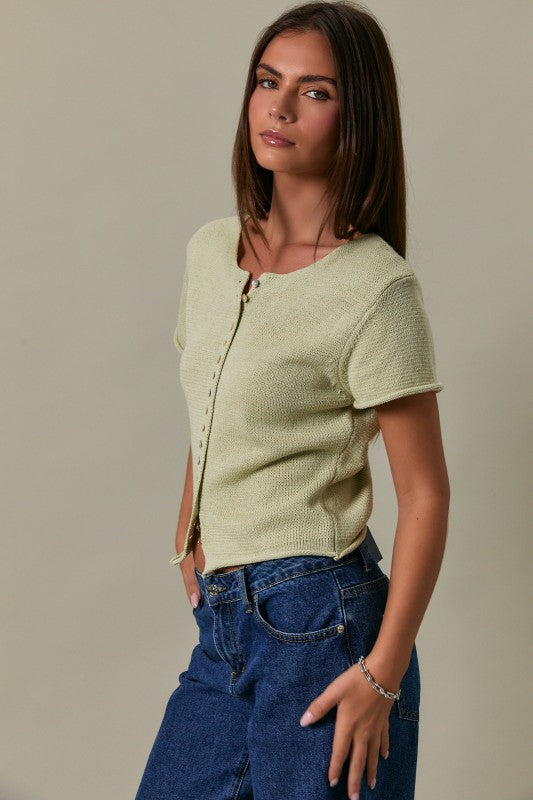 Woman wearing a light green knitted cardigan and blue jeans against a neutral background