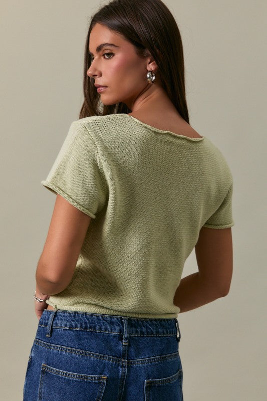 Woman wearing a light green knitted top and blue jeans against a neutral background