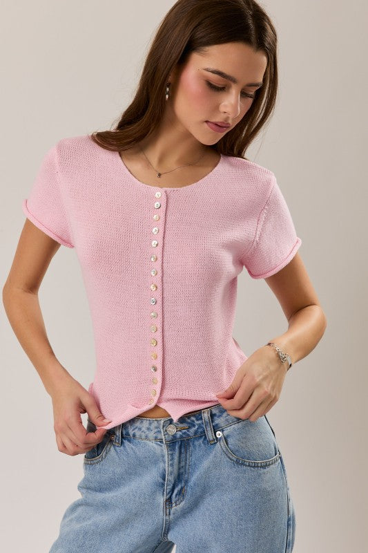 Woman wearing a pink short-sleeve button-up top and blue jeans on a plain background