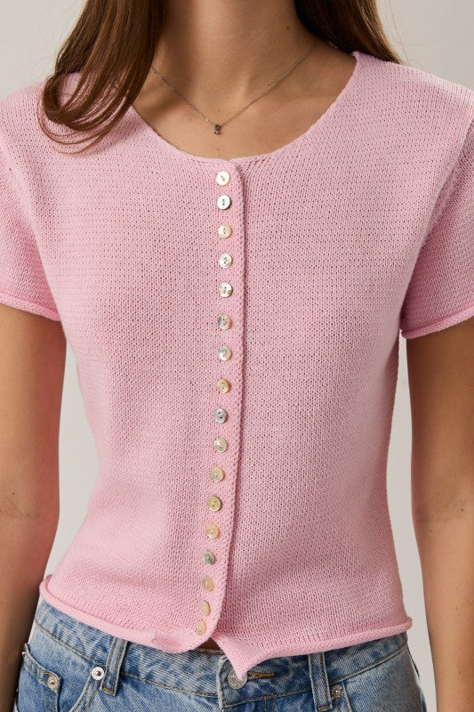 Pink knitted top with button details worn by a person, against a neutral background