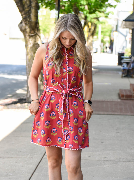 Woman wearing a red floral dress on a sidewalk with trees and buildings in the background