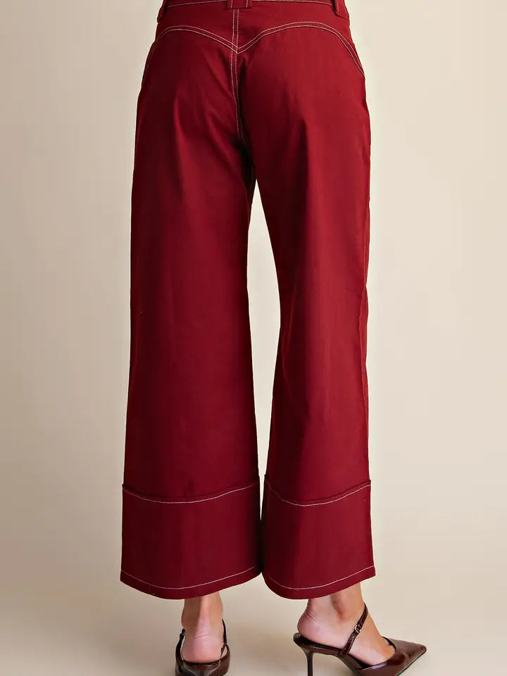 A pair of wide-leg cropped pants in deep burgundy red, shown from the back on a model wearing brown pointed-toe mule heels against a solid beige background.