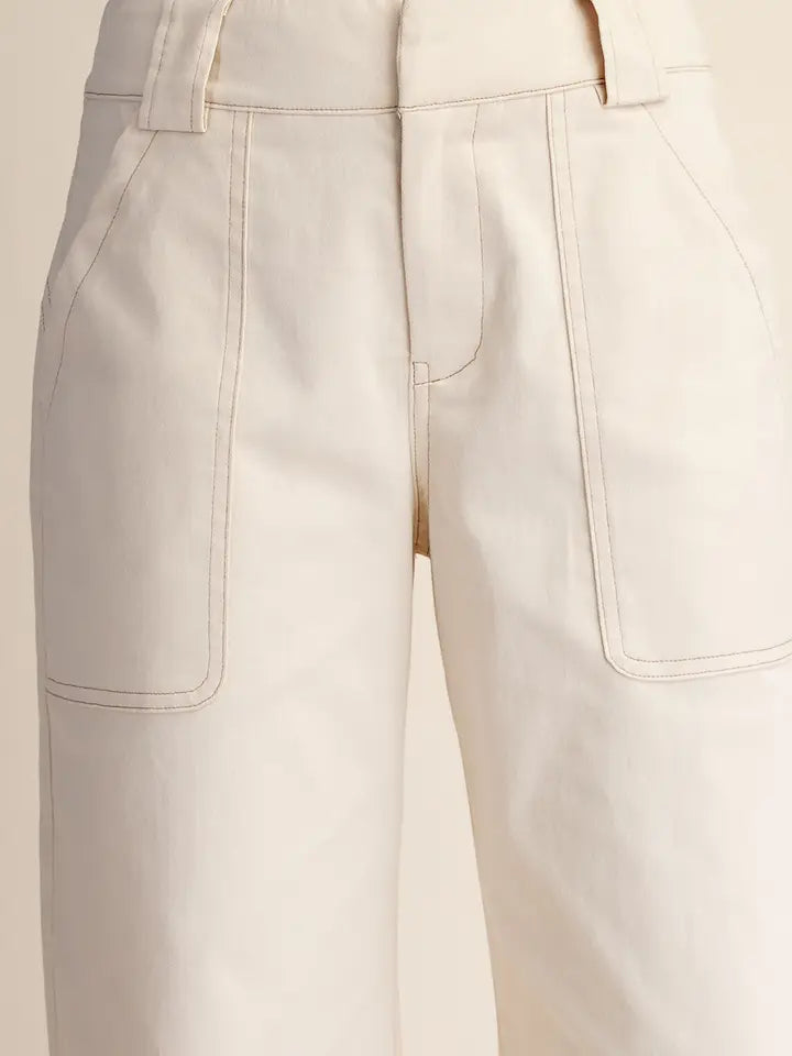 Close-up of a pair of off-white or cream wide-leg trousers, showing the front waistband, belt loops, and large front patch pockets with contrast stitching.