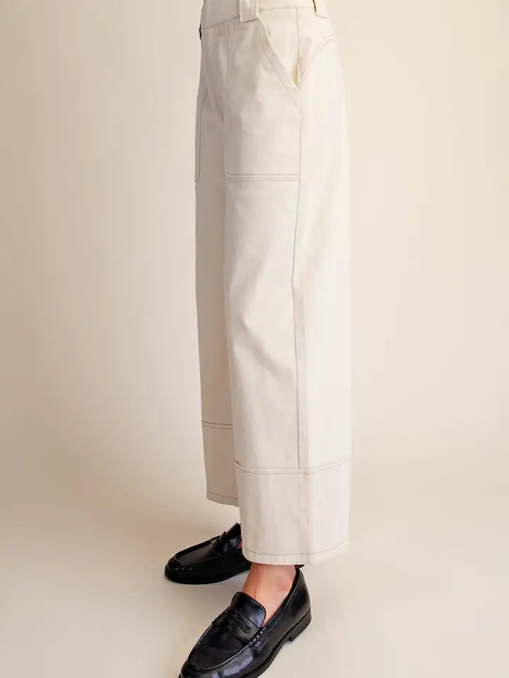A person wearing off-white cropped wide-leg trousers and black leather loafers, shown from the waist down against a plain beige studio background.