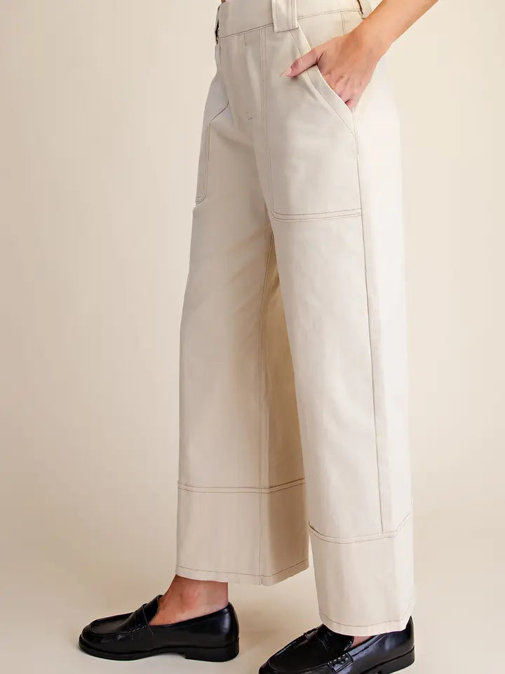 A person wearing off-white cropped wide-leg pants with side pockets and black loafers, shown from the waist down against a plain beige studio background.
