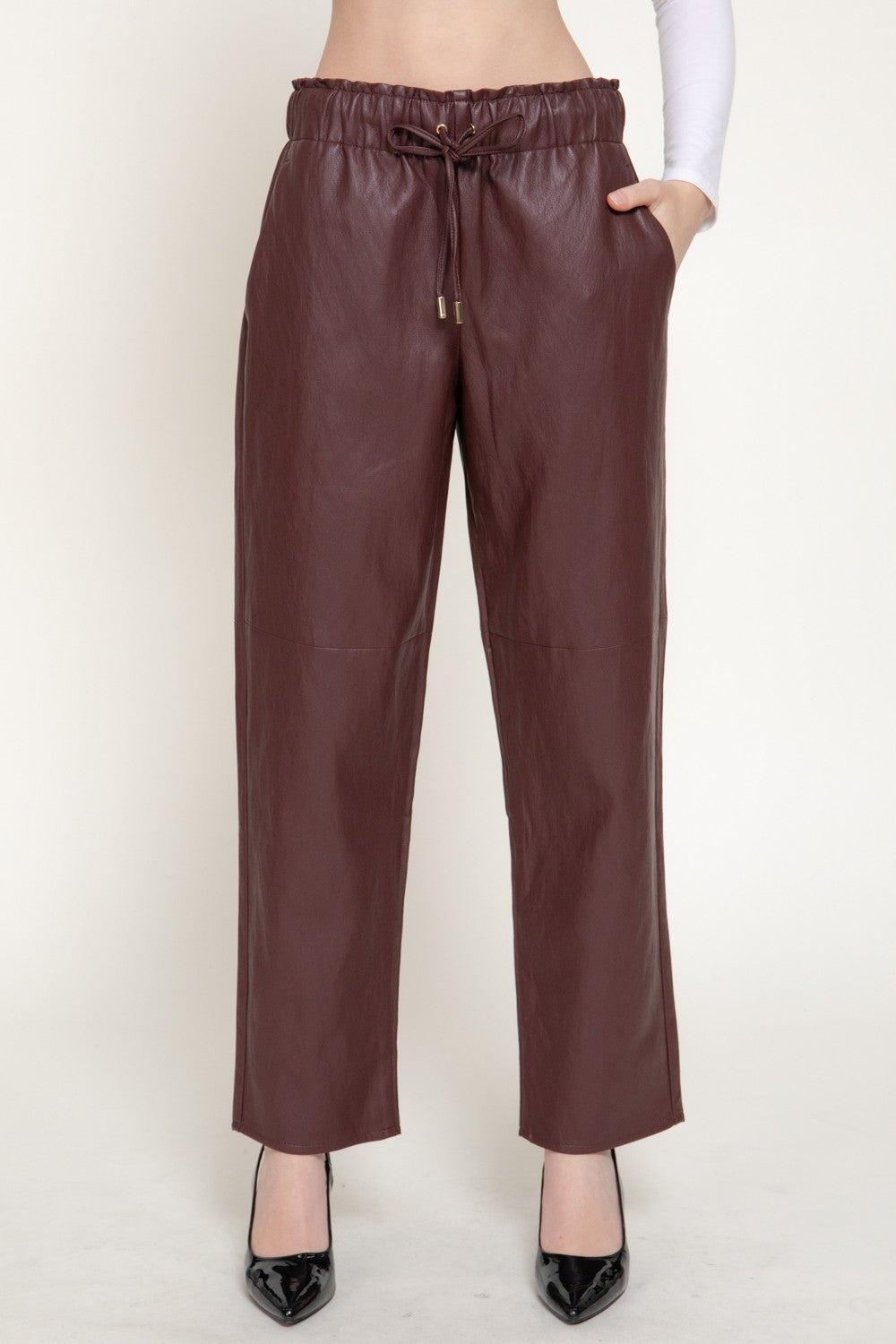 A person wearing wide-leg brown faux-leather pants with an elastic drawstring waist, paired with black pointed-toe heels against a plain light background.