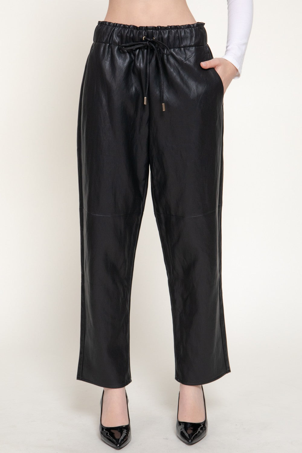 Black faux leather wide-leg cropped pants with an elastic drawstring waist, modeled with black pointed-toe heels against a plain off-white studio background.