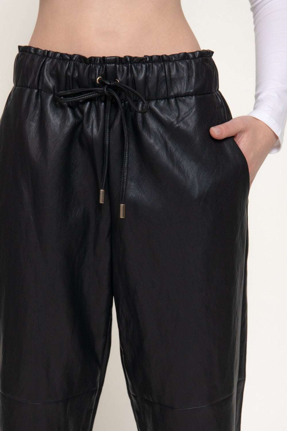 Black faux leather drawstring pants with side pockets, shown on a model against a plain white background.
