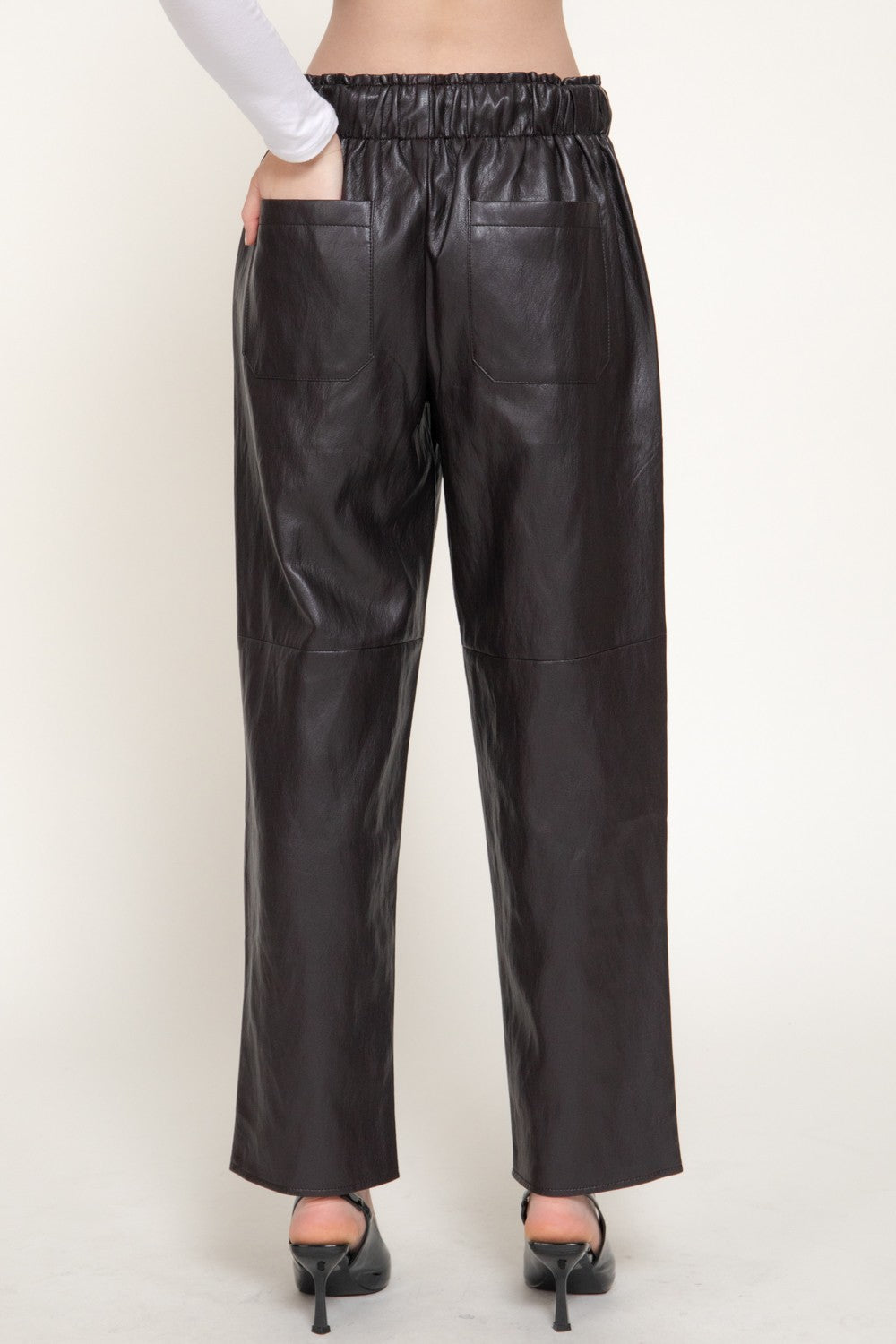 Black faux leather wide-leg pants with an elastic waistband, shown on a model from the back against a light beige studio background.