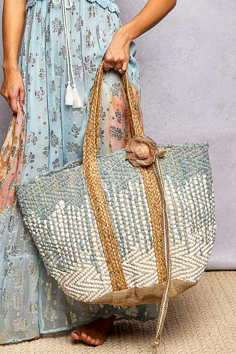 Person holding a textured handbag with floral design and flower detail.