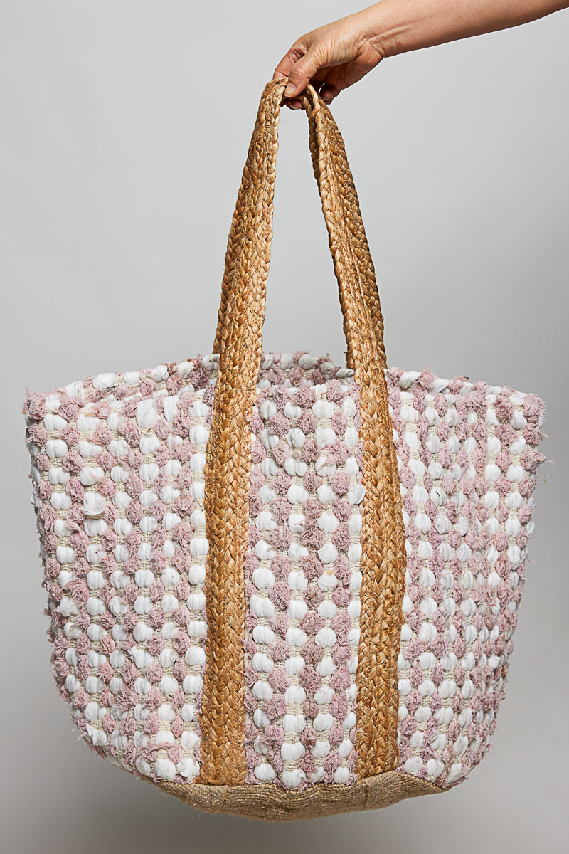 Hand holding a woven bag with pink, white, and beige pattern against a gray background