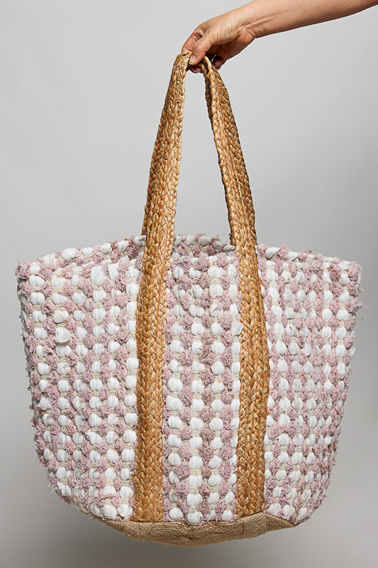 Hand holding a woven bag with pink, white, and beige pattern against a gray background