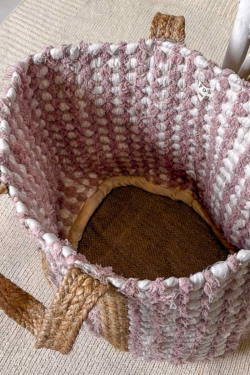 Textured pink and brown woven basket with a wooden handle on a beige surface