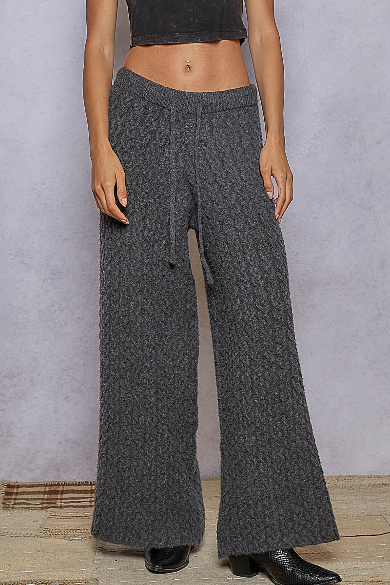 Person wearing gray knitted pants against a plain background