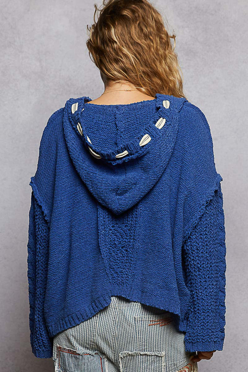 Person wearing a blue knitted hoodie with a hood on a gray background