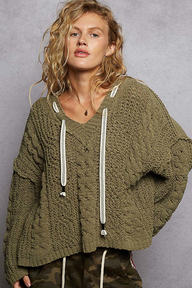 Woman wearing a green knitted sweater with white drawstrings against a gray background