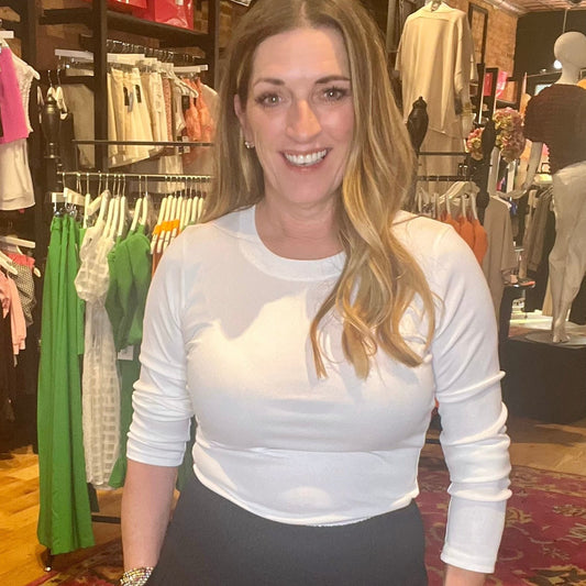 Woman in a white long-sleeve top standing in a clothing store.