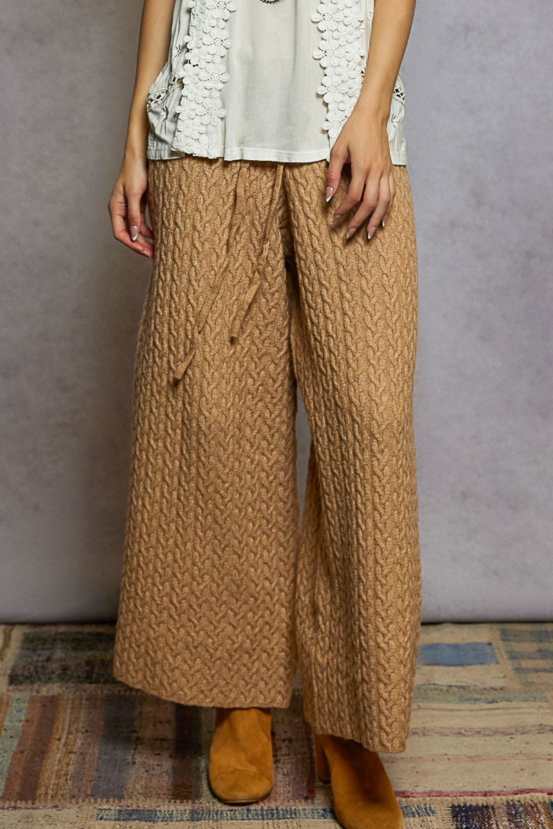 Person wearing brown knitted pants with a plain background
