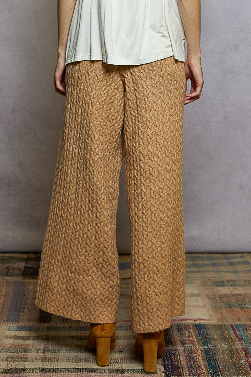 Person wearing brown textured pants and a light-colored top against a gray wall.