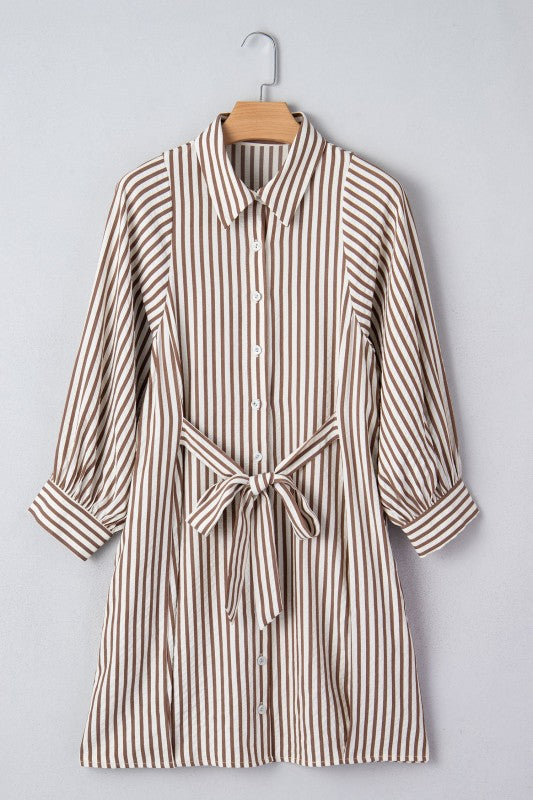 Striped shirt dress with a belt on a hanger against a gray background