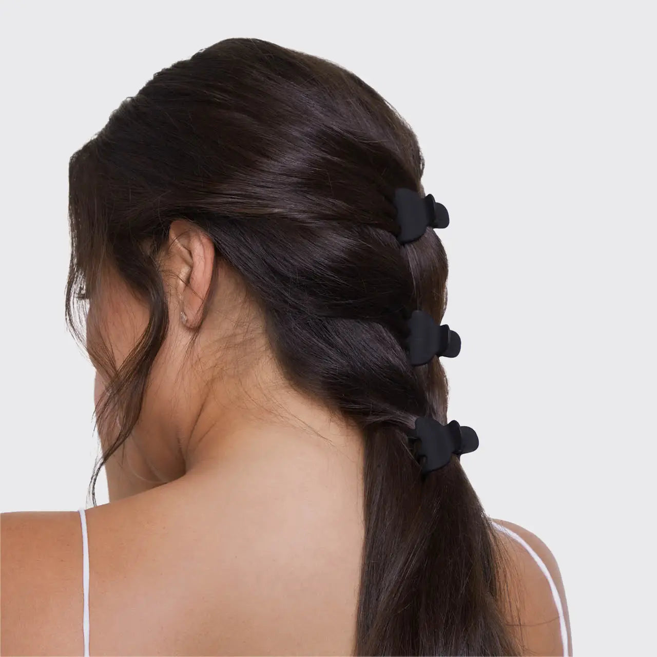 Woman with a ponytail held in place by black hair ties on a white background