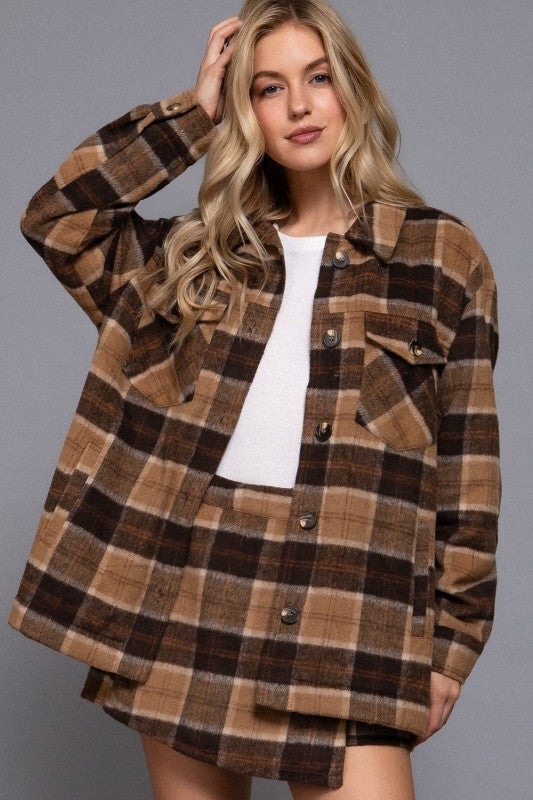Woman wearing a brown plaid jacket over a white shirt on a gray background