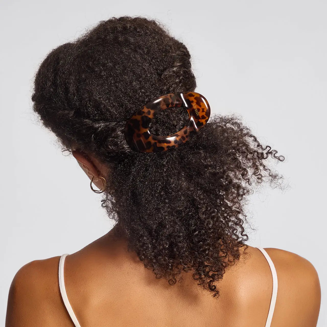 Person with curly hair wearing a leopard print hair tie on a plain background