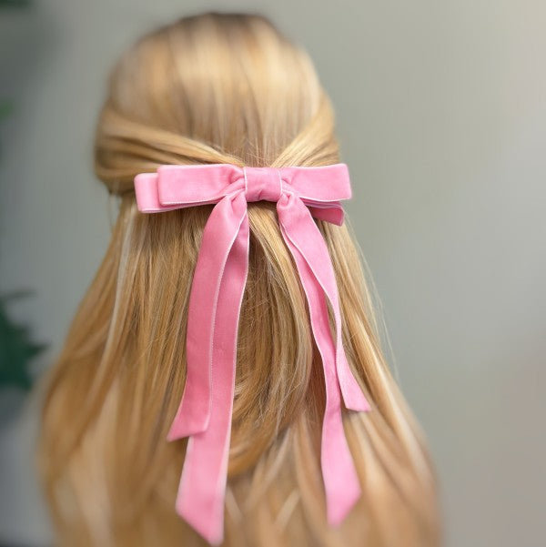 Pink hair bow on a person with blonde hair against a neutral background