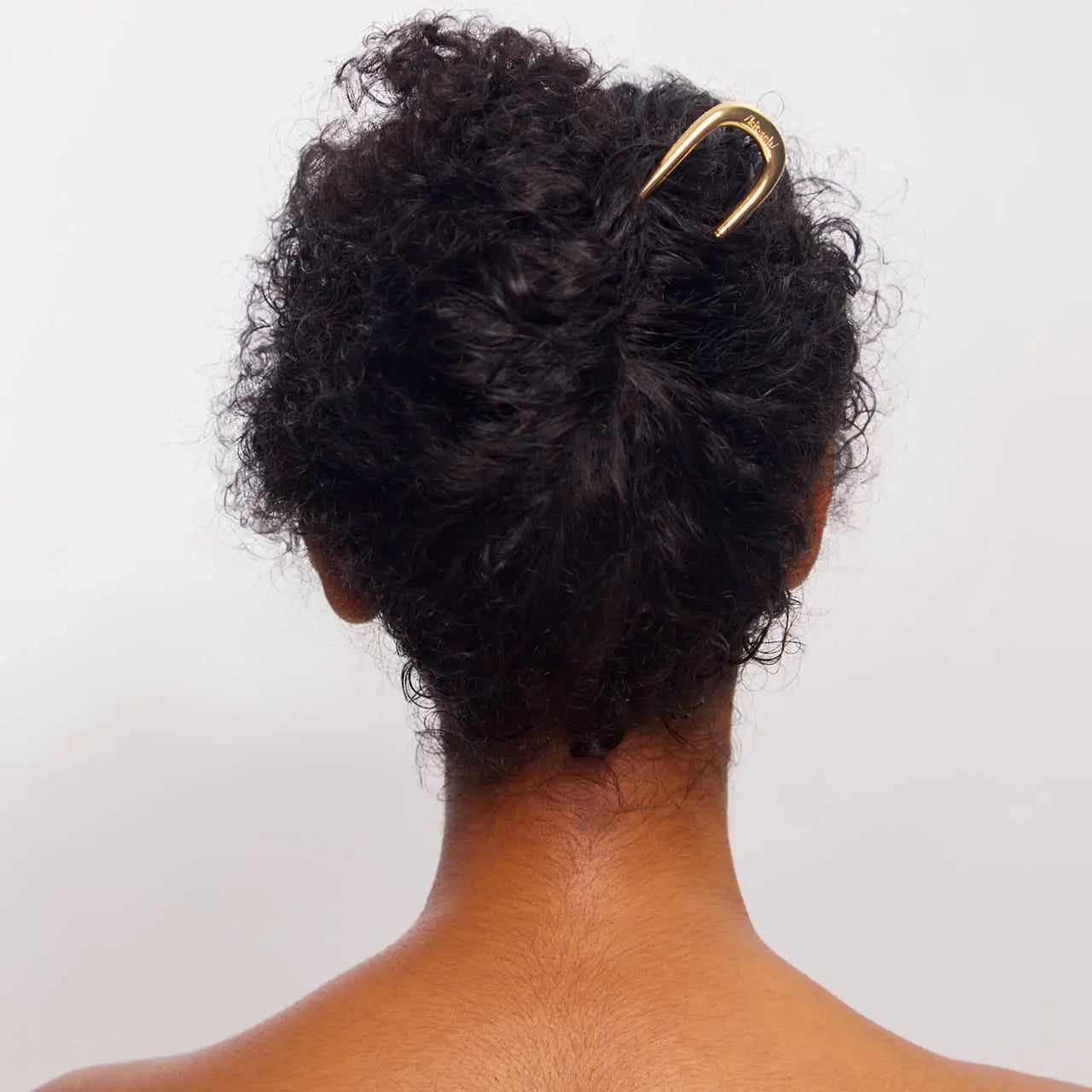 Person with styled hair using a gold hair clip on a plain background
