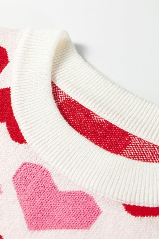 Close-up of a white sweater with red and pink heart patterns on a light gray background