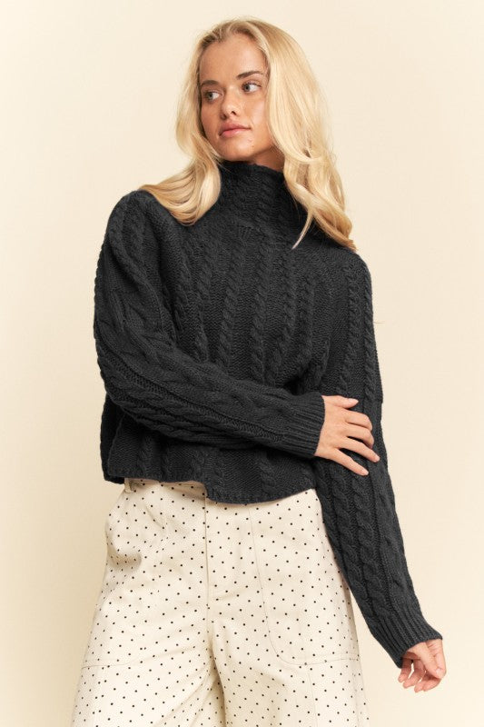 Woman wearing a black cable knit sweater with white polka dot pants on a beige background