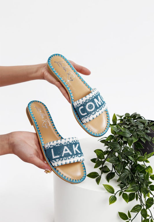 Blue sandals with white text held by a person, plant in the background