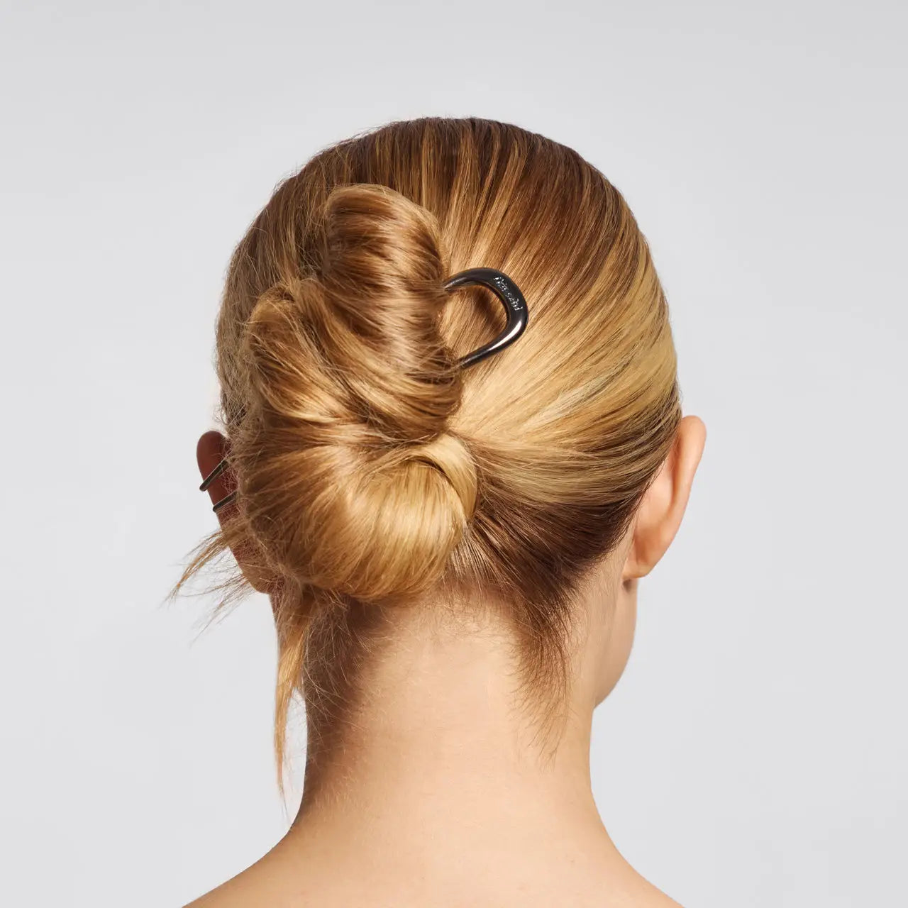 Back view of a person with a neatly styled bun using a hair clip on a plain background