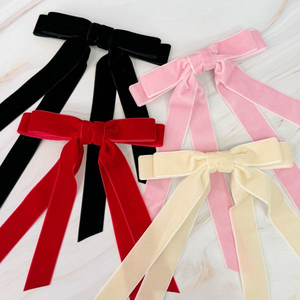 Set of black, red, pink, and beige velvet bows on a light wooden surface.