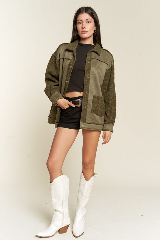 Woman wearing an olive green jacket, black top, and white boots on a plain background