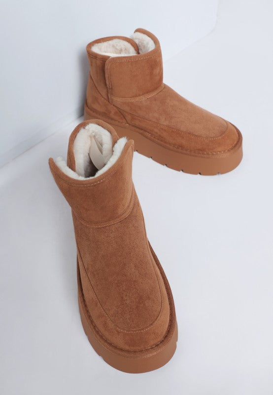 Pair of brown suede boots with white fur lining on a light gray background