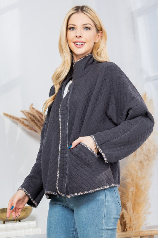 Woman wearing a dark gray quilted jacket with white trim against a light background