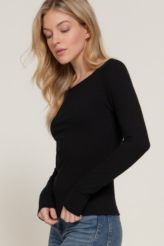 Woman wearing a black long-sleeve top and blue jeans on a beige background