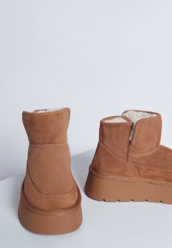 Pair of brown suede boots with white fur lining on a light gray background