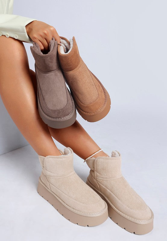 Person wearing beige and brown ankle boots on a light gray background