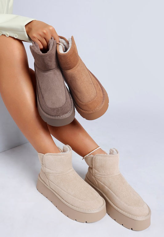 Person wearing beige and brown ankle boots on a light gray background