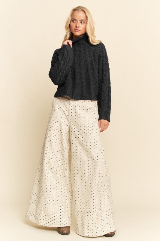 Woman wearing a dark sweater and white patterned skirt against a beige background