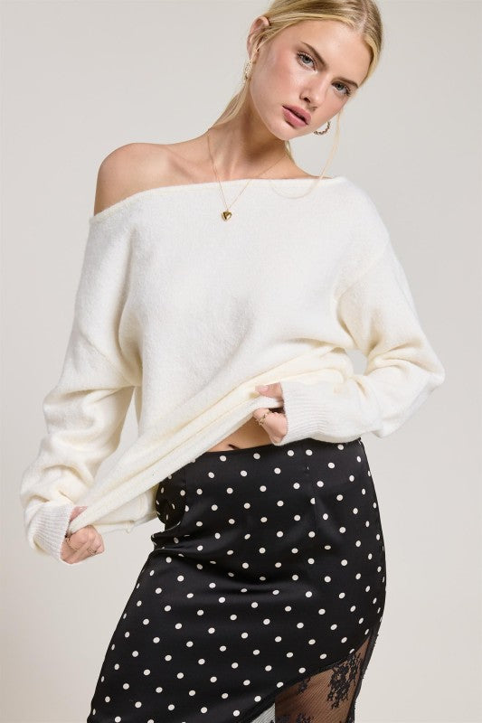 Woman wearing a white off-shoulder sweater and black polka dot skirt on a plain background