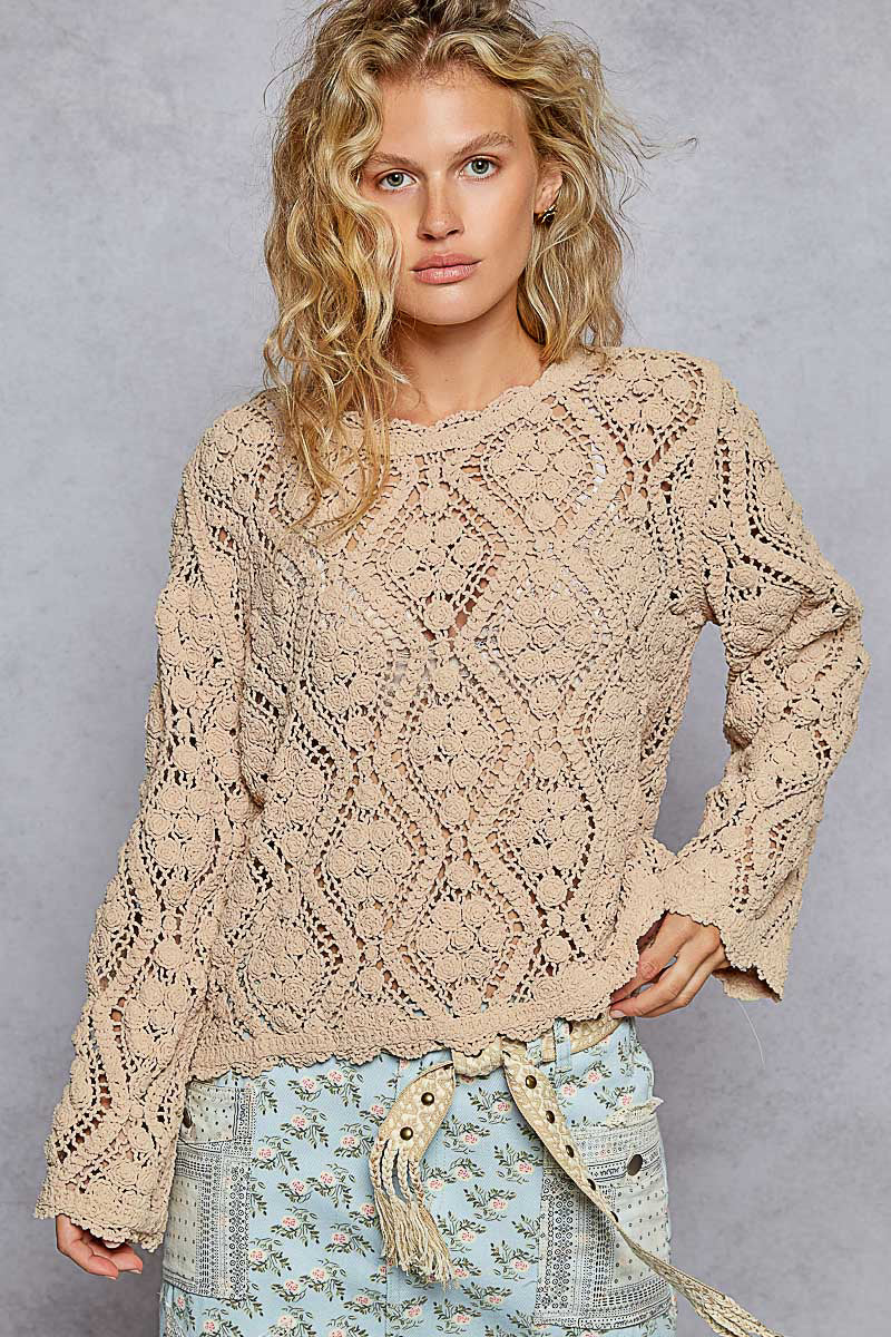 Woman wearing a beige lace sweater against a gray background