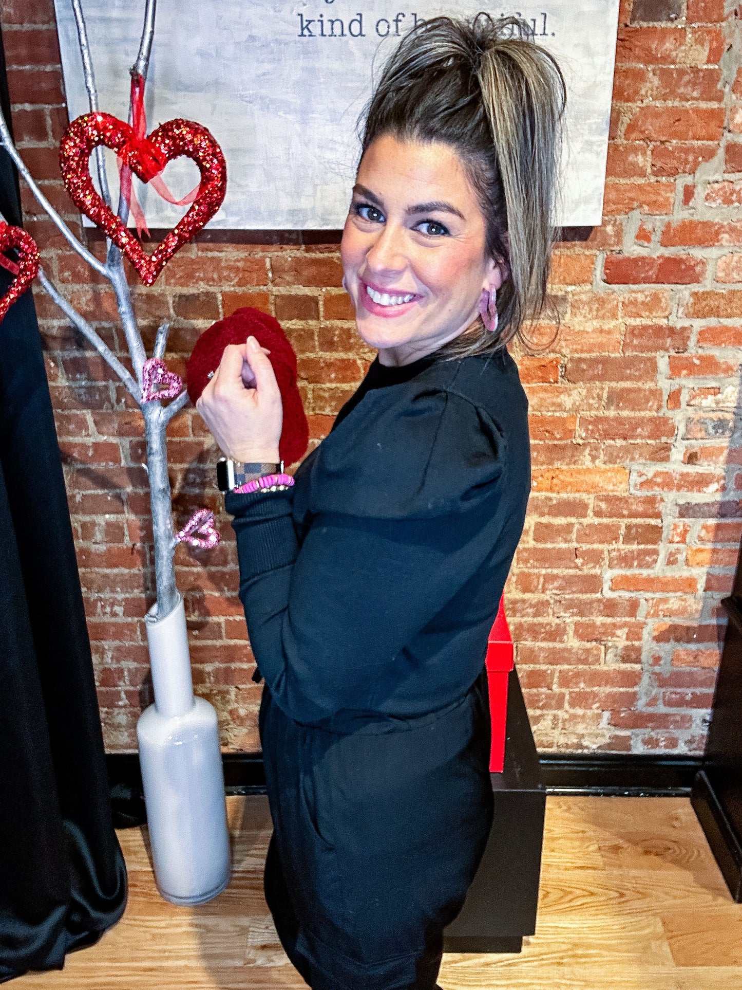 A woman wearing a black puff sleeve sweater top with black pants, accessorized with multiple bracelets and earrings.